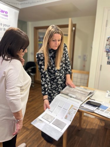 Two ladies look at the contents of a brochure containing kitchen designs